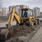 Б/у экскаватор-погрузчик копает траншею на строительной площадке